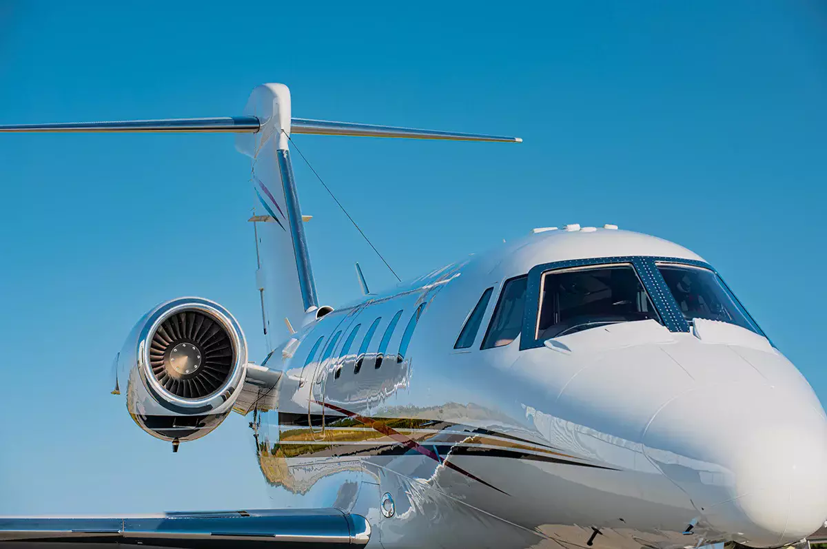 Close-up of a white private jet on a runway under a clear blue sky, showing the cockpit, side windows and rear engine.