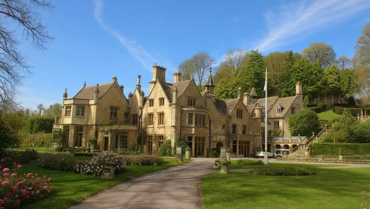 Historic country house set within landscaped gardens, with a long driveway, stone architecture and surrounding greenery.